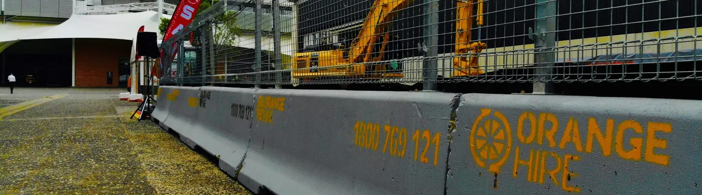 Barreras de seguridad para concreto alineadas en un sitio de construcción, suministradas por Orange Hire para la protección del tráfico y del sitio.