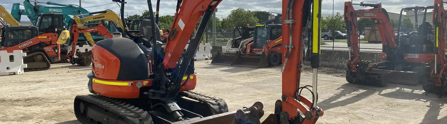 Línea de excavadoras usadas en exhibición en un patio de construcción, con señales de seguridad y barreras que marcan el área de visualización.