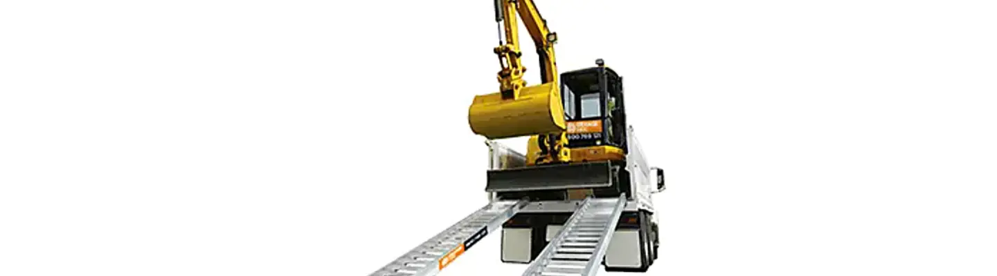 Una excavadora compacta colocada sobre una rampa de remolque, lista para cargar o transportar sobre un fondo plano.