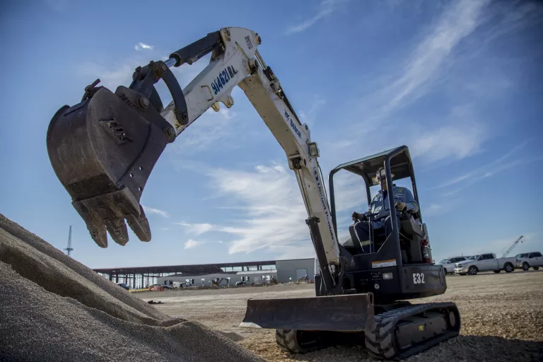 Miniexcavadora con brazo extendido cerca de una pila de tierra
