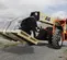 Vista frontal en ángulo de un manipulador telescópico JLG anaranjado y tostado con un aditamento para montacargas que levanta un palé al aire libre.
