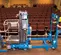 Vista lateral de un kit de aplanadora Genie azul para elevador de rueda de empuje con el brazo retraído, inactivo en un escenario en un auditorio.