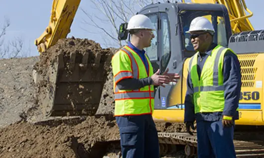 dos hombres con cascos en un sitio de construcción con excavadora 
