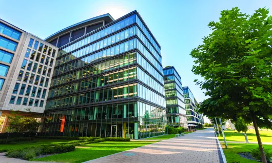 imagen de archivo del exterior de un edificio de oficinas de vidrio cerca de árboles bajo un cielo azul