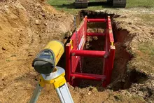 Pipe laser operating in trench with protective blue shield for pipe alignment             